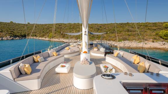 Luxuriöser Sitzbereich mit Kissen und Tischen auf dem Deck der Lady Gita vor malerischer Küste.